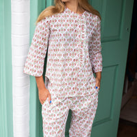 A woman wearing a matching two-piece pajama set with a white base and a pink and green floral block print, standing in front of a mint green door.