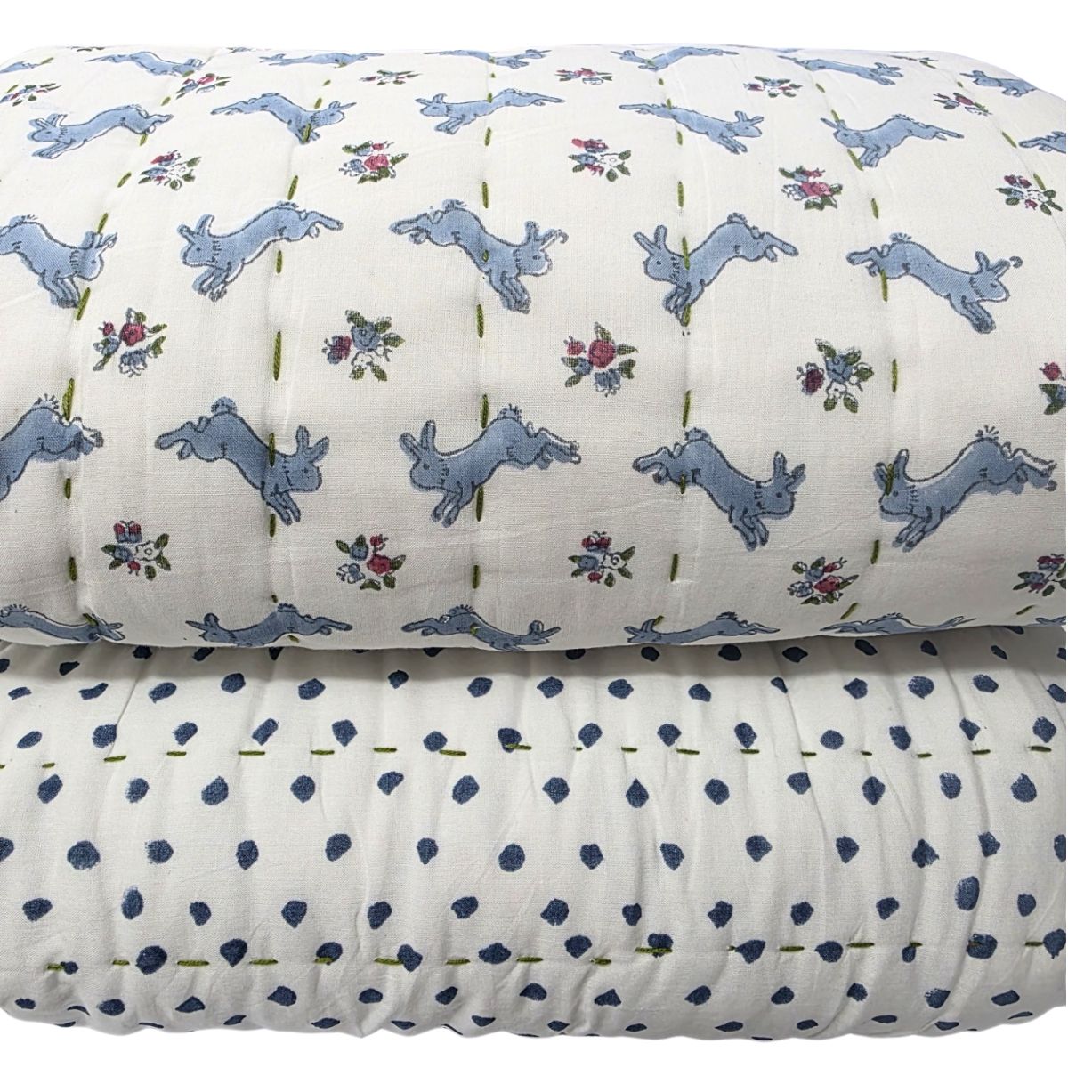 A folded white quilted bedding set featuring a top layer with a light blue rabbit print and small floral motifs, and a bottom layer with dark blue polka dots.