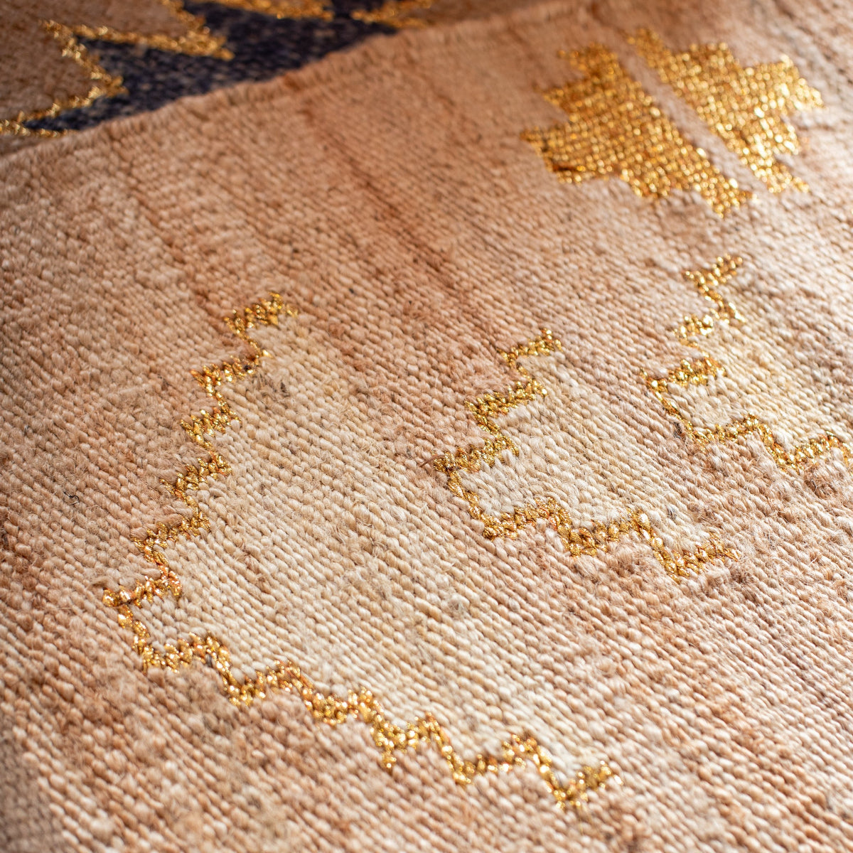 Close-up of a textured jute with gold embroidery on a beige background