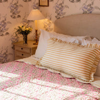 Bedroom with floral wallpaper, bed with striped pillow, and nightstand with lamp and flowers.