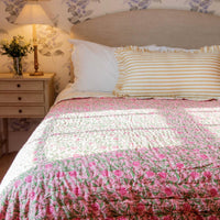 Bed with floral bedding and striped pillow, nightstand with lamp in a bedroom setting.