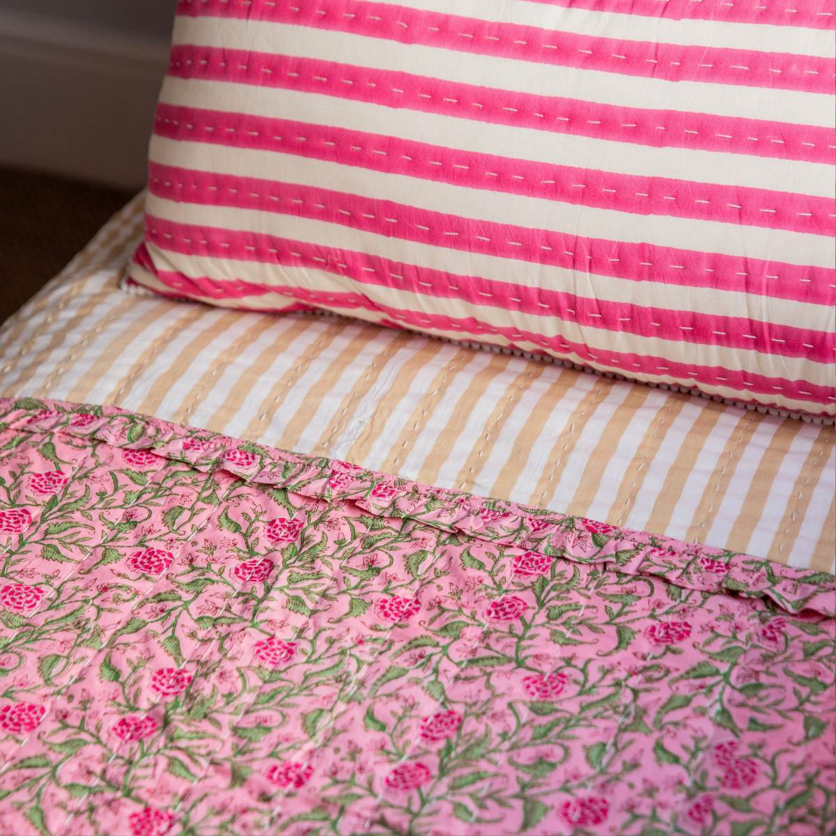 Close-up of pink floral quilt and striped pillow on a bed.