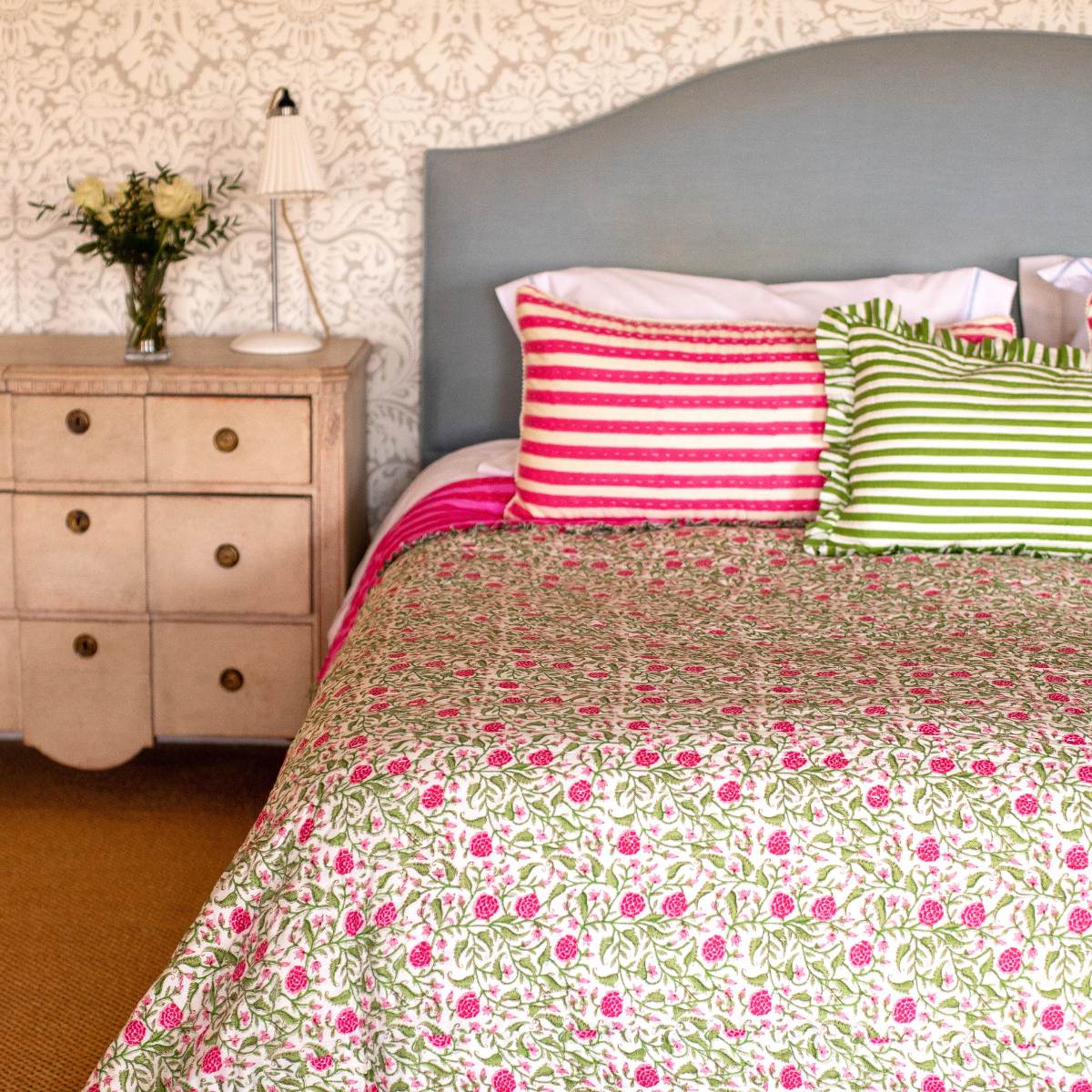 Bedroom with floral bedspread, striped pillows, and a nightstand.