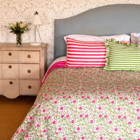 Bedroom with floral bedspread, striped pillows, and a nightstand.