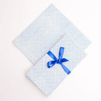 A folded white napkin with blue polka dot blockprint and a blue ribbon bow on top, on a white background.