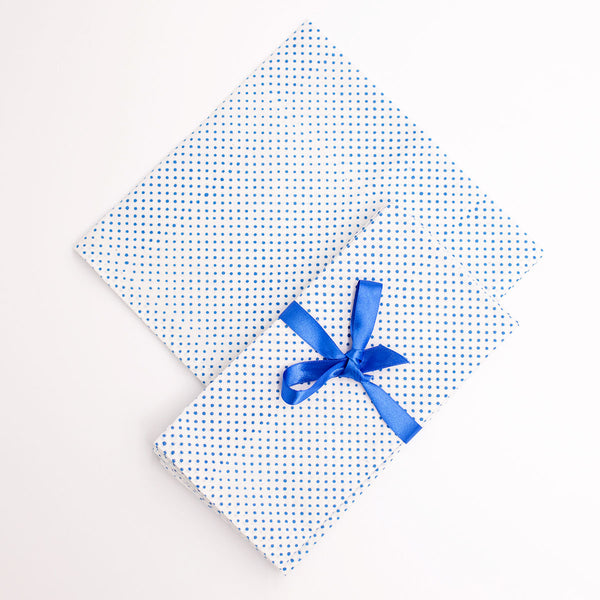 A folded white napkin with blue polka dot blockprint and a blue ribbon bow on top, on a white background.