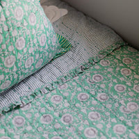 Green and white floral patterned bedding on a bed with a pillow.