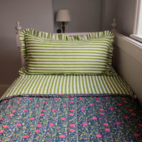 Bed with green and white striped bedding and a floral quilt in a bedroom setting.