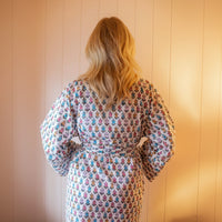 Woman wearing a floral dress standing against a wooden paneled wall.