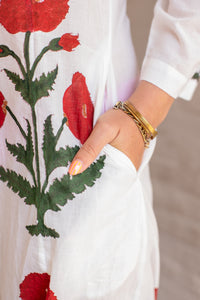 White garment with red floral embroidery and a gold bracelet on a neutral background